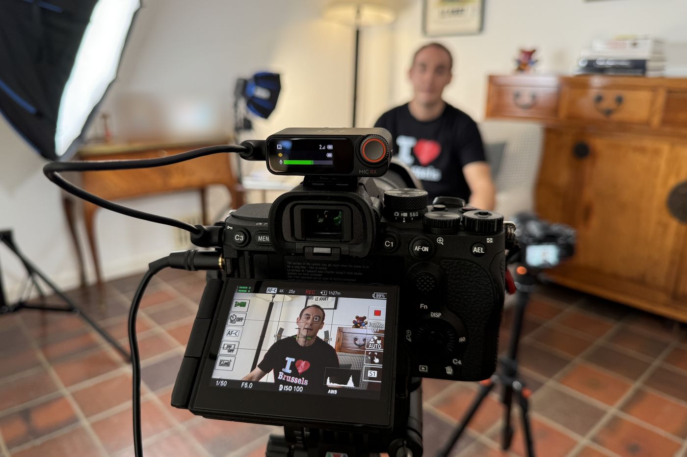 Vidéaste en tournage d'interview chez un client : caméra en enregistrement avec micro sans fil, invité interviewé en arrière-plan